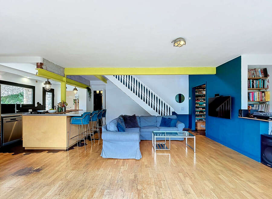 This open-concept living space features a modern kitchen with a large island and bar stools, flowing seamlessly into a comfortable living area with a sectional sofa and glass coffee table.