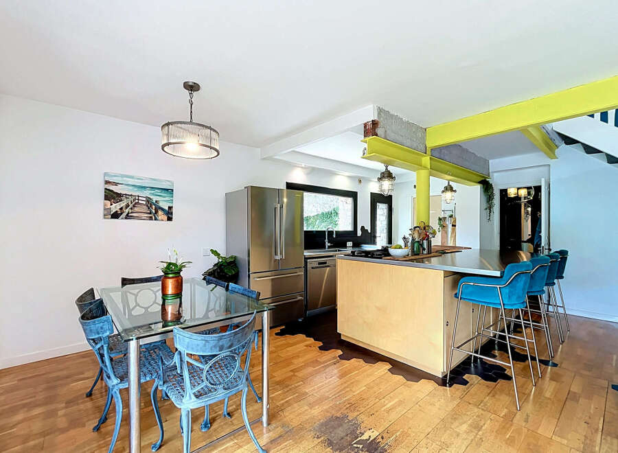 This modern kitchen and dining area features a sleek stainless steel refrigerator, a spacious island with bar seating, and a glass-top dining table with ornate chairs.