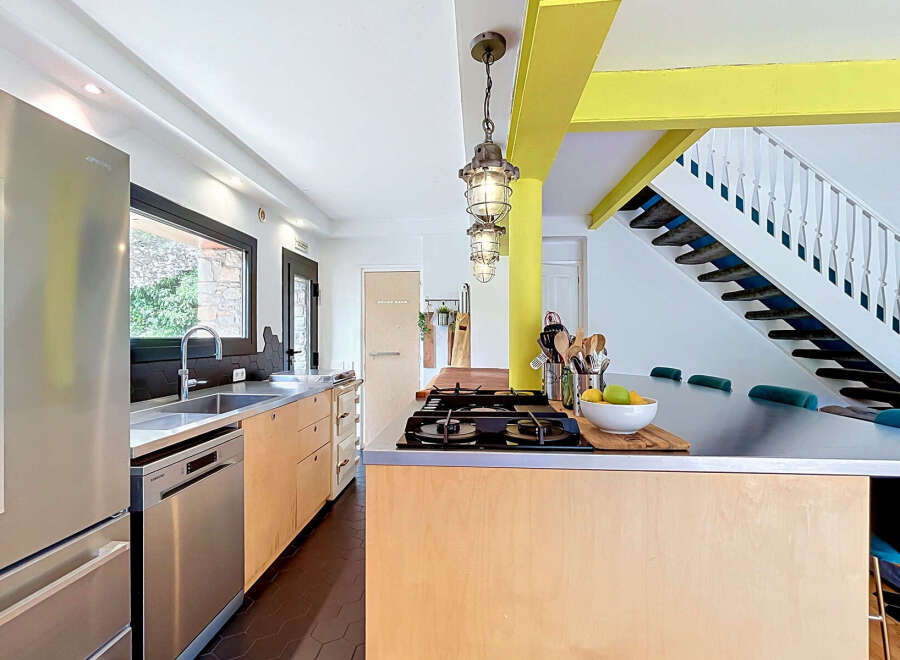 This modern kitchen features a sleek stainless steel refrigerator and dishwasher, complemented by light wood cabinetry and a durable metal countertop.