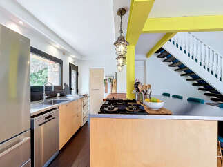 This modern kitchen features a sleek stainless steel refrigerator and dishwasher, complemented by light wood cabinetry and a durable metal countertop.