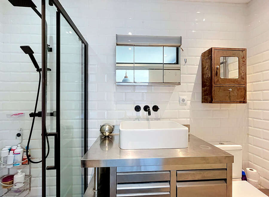 This modern bathroom features a sleek stainless steel vanity with a vessel sink and black fixtures, complemented by a glass-enclosed shower with a rainfall showerhead.