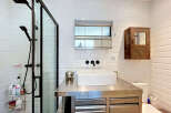 This modern bathroom features a sleek stainless steel vanity with a vessel sink and black fixtures, complemented by a glass-enclosed shower with a rainfall showerhead.