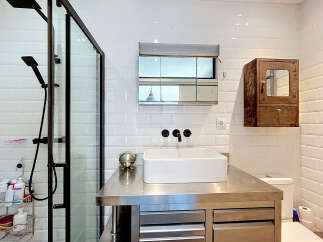 This modern bathroom features a sleek stainless steel vanity with a vessel sink and black fixtures, complemented by a glass-enclosed shower with a rainfall showerhead.