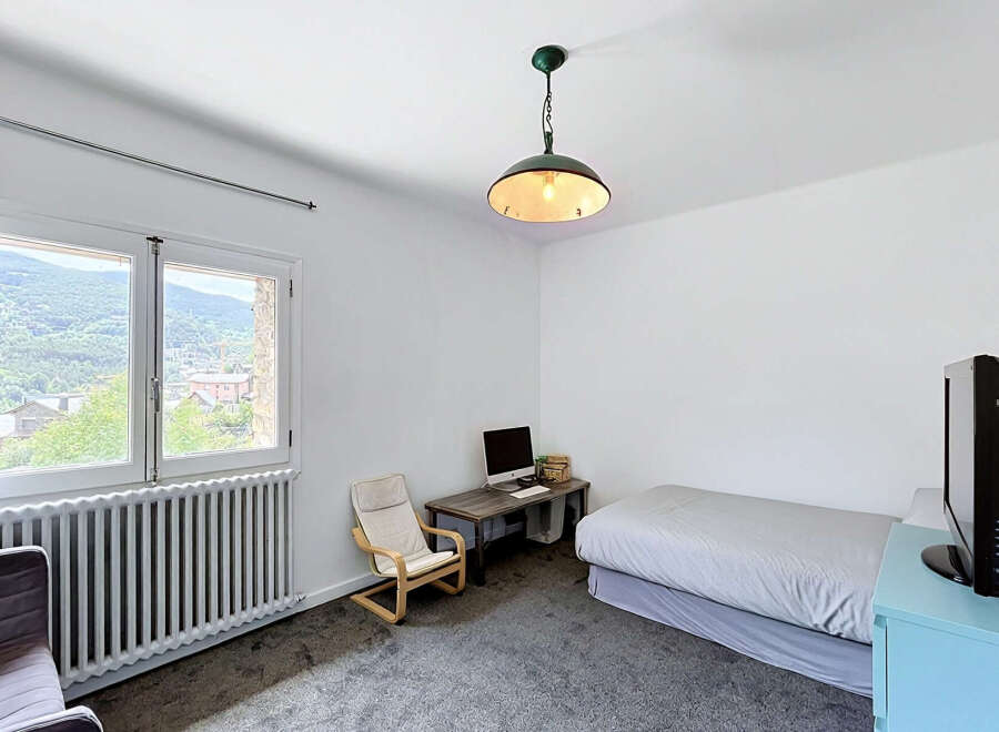 This bedroom offers a comfortable and functional space, featuring a cozy bed, a dedicated workspace with a computer, and a relaxing armchair.
