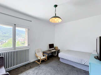 This bedroom offers a comfortable and functional space, featuring a cozy bed, a dedicated workspace with a computer, and a relaxing armchair.