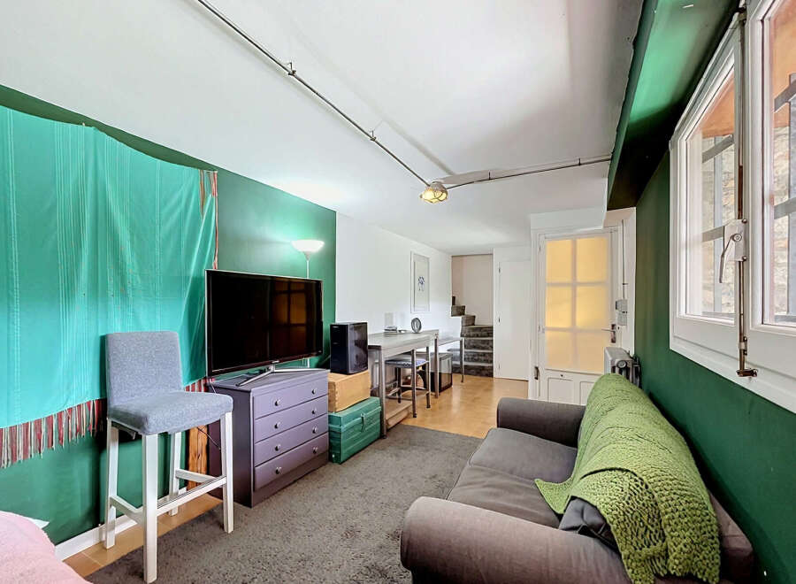 This living space features a modern entertainment setup with a large flat-screen TV and a stylish purple dresser, complemented by a comfortable grey sofa adorned with a vibrant green throw blanket.
