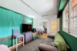 This living space features a modern entertainment setup with a large flat-screen TV and a stylish purple dresser, complemented by a comfortable grey sofa adorned with a vibrant green throw blanket.