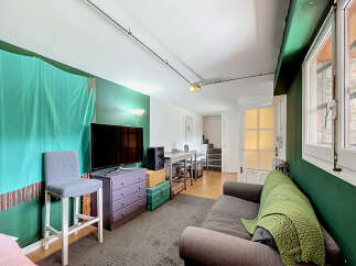 This living space features a modern entertainment setup with a large flat-screen TV and a stylish purple dresser, complemented by a comfortable grey sofa adorned with a vibrant green throw blanket.