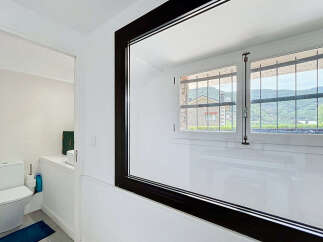This modern bathroom features a sleek toilet and a large mirror reflecting a picturesque view of the surrounding hills and houses through a barred window.
