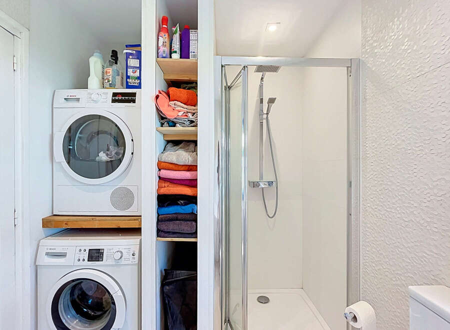 This compact bathroom maximizes space with a stacked Bosch washer and dryer, perfect for smaller homes or apartments.