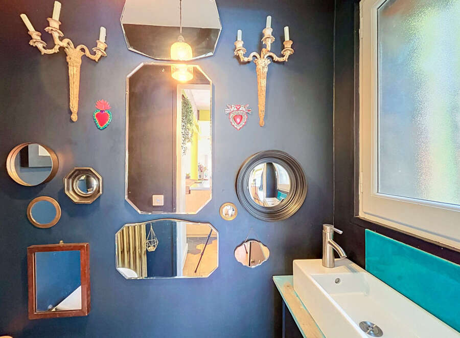 This eclectic bathroom features a striking gallery wall adorned with an assortment of decorative mirrors and vintage sconces, creating a unique focal point.