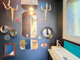 This eclectic bathroom features a striking gallery wall adorned with an assortment of decorative mirrors and vintage sconces, creating a unique focal point.