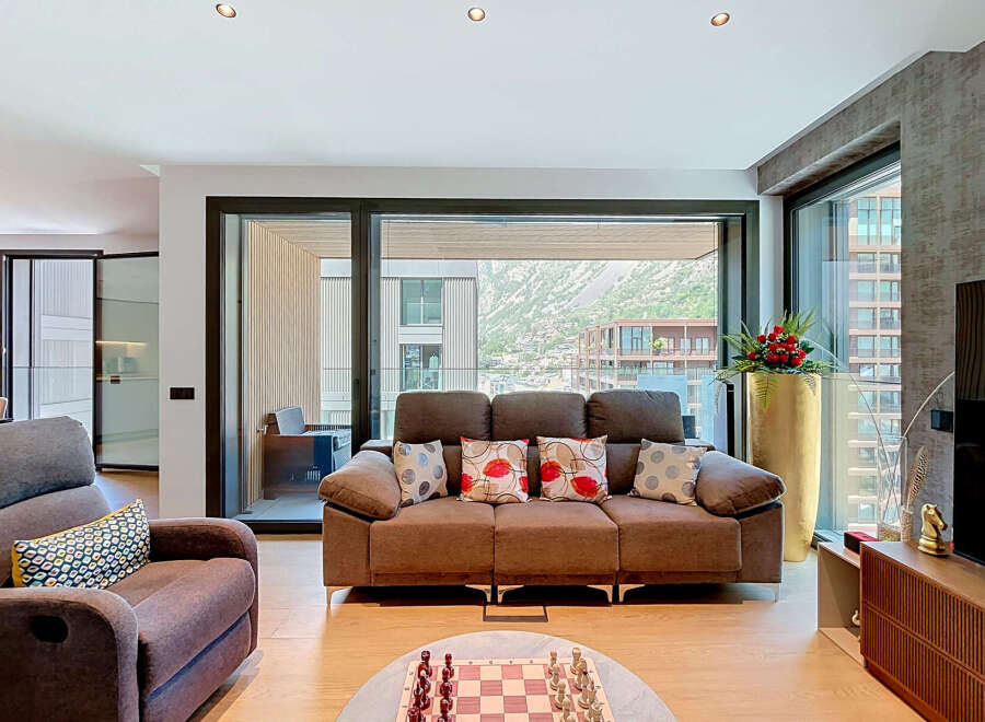 Experience modern living in this spacious living room, featuring a comfortable brown sofa adorned with decorative pillows and a large sliding glass door offering stunning mountain views.