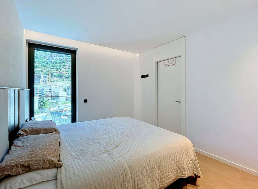 Experience modern comfort in this beautifully appointed bedroom, featuring a plush bed with elegant pillows and a large window offering stunning city and mountain views.