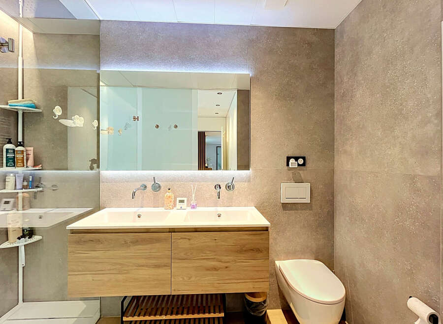 Experience modern luxury in this stunning bathroom featuring a sleek double vanity with ample storage and a large, illuminated mirror.