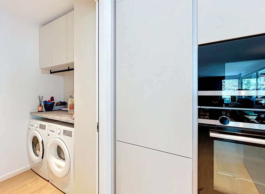 Discover this modern laundry room featuring stacked white appliances, including a washer and dryer, complemented by ample cabinet storage above.