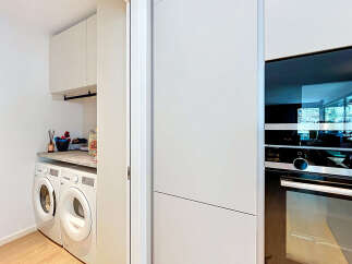 Discover this modern laundry room featuring stacked white appliances, including a washer and dryer, complemented by ample cabinet storage above.