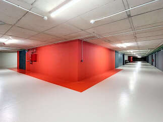 Discover this modern and well-lit underground parking space, featuring a striking red accent wall and a clean, white epoxy floor.