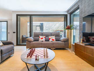 Experience modern living in this stylish apartment, featuring a spacious living area with a comfortable sofa and a large window offering scenic views.