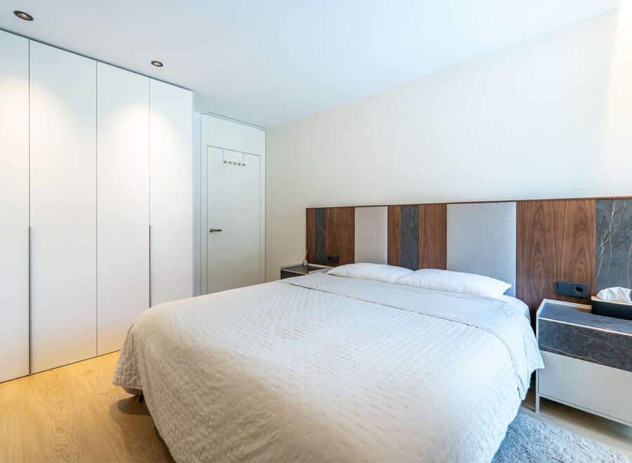 This modern bedroom features a large, comfortable bed with a textured white comforter, complemented by a stylish headboard with wood and fabric panels.