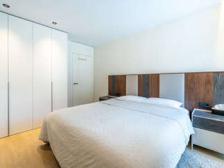 This modern bedroom features a large, comfortable bed with a textured white comforter, complemented by a stylish headboard with wood and fabric panels.