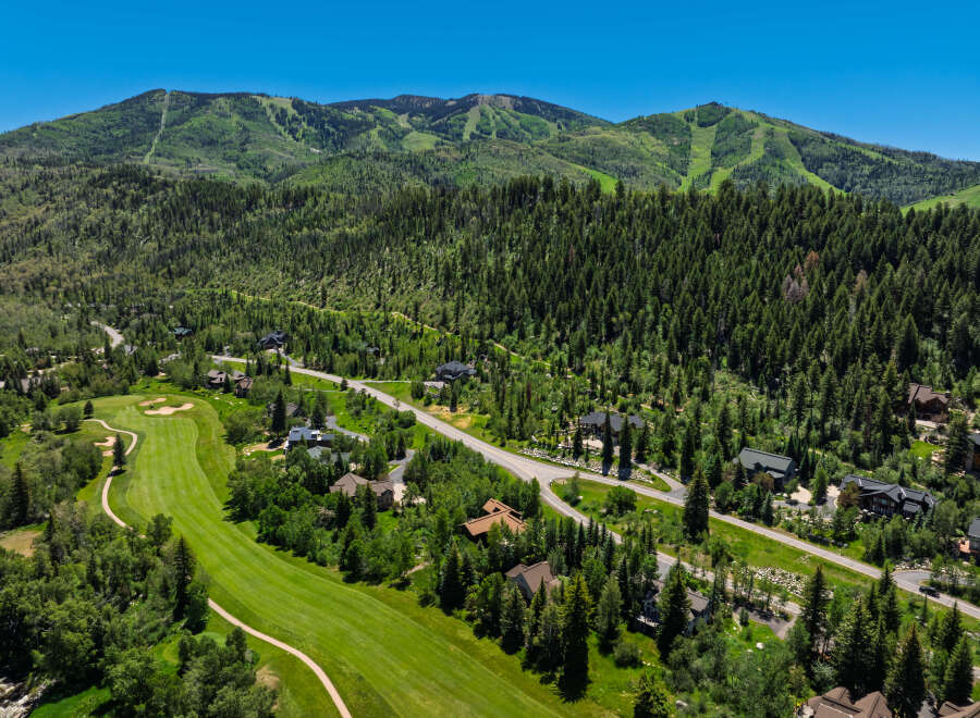 Experience luxury mountain living with this stunning aerial view of a sprawling estate nestled amidst lush greenery and majestic peaks.
