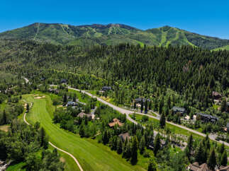 Experience luxury mountain living with this stunning aerial view of a sprawling estate nestled amidst lush greenery and majestic peaks.