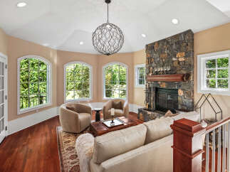 Experience luxurious living in this stunning living room, featuring a grand stone fireplace and a unique, artistic chandelier.