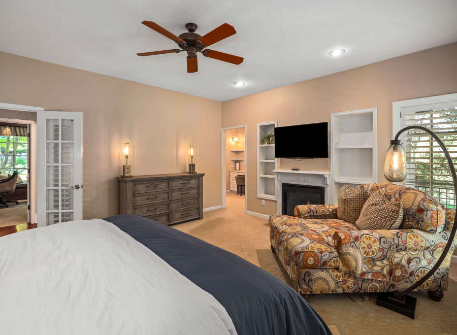 Experience ultimate comfort in this luxurious bedroom, featuring a cozy seating area with a patterned chaise lounge and a modern fireplace.