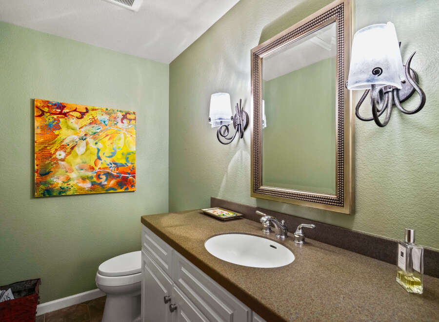 This powder room features a vibrant abstract painting on a light green textured wall, complementing the elegant vanity with a granite countertop and a white undermount sink.