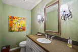 This powder room features a vibrant abstract painting on a light green textured wall, complementing the elegant vanity with a granite countertop and a white undermount sink.