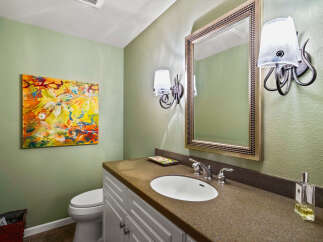 This powder room features a vibrant abstract painting on a light green textured wall, complementing the elegant vanity with a granite countertop and a white undermount sink.