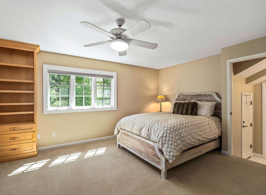 This charming bedroom features a comfortable bed with a patterned duvet and a rustic headboard, complemented by a wooden bookshelf and a large window offering natural light.