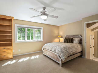 This charming bedroom features a comfortable bed with a patterned duvet and a rustic headboard, complemented by a wooden bookshelf and a large window offering natural light.