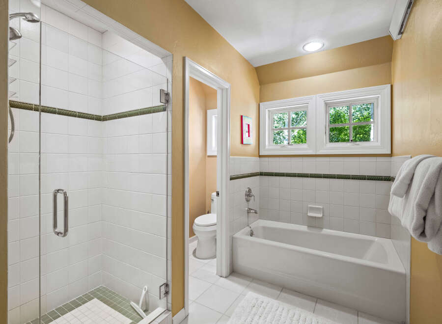 This charming bathroom features a spacious glass-enclosed shower with white tiled walls and a decorative green accent stripe.