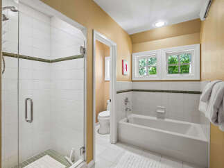 This charming bathroom features a spacious glass-enclosed shower with white tiled walls and a decorative green accent stripe.