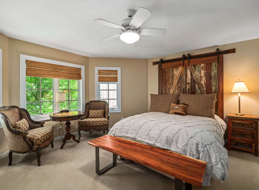 Experience rustic charm in this inviting bedroom, featuring a unique barn door headboard and a cozy seating area by the bay window.