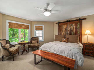 Experience rustic charm in this inviting bedroom, featuring a unique barn door headboard and a cozy seating area by the bay window.