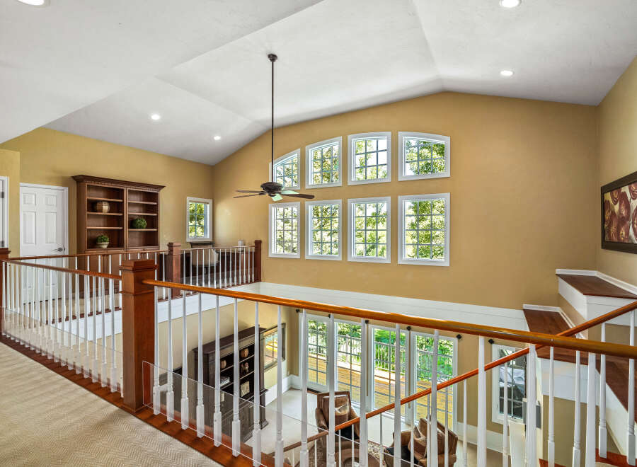 This stunning home features a grand entryway with a vaulted ceiling and a beautiful wooden banister overlooking the living area.