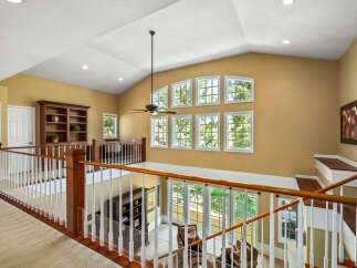 This stunning home features a grand entryway with a vaulted ceiling and a beautiful wooden banister overlooking the living area.