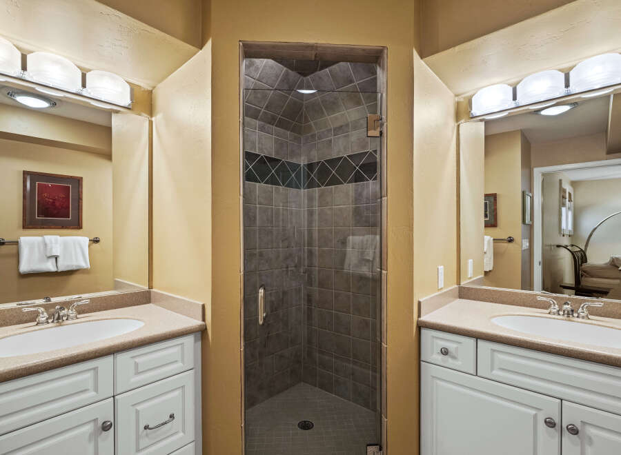 This bathroom features a spacious walk-in shower with elegant tilework, complemented by dual vanities with granite countertops.