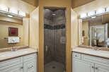 This bathroom features a spacious walk-in shower with elegant tilework, complemented by dual vanities with granite countertops.