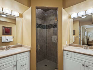 This bathroom features a spacious walk-in shower with elegant tilework, complemented by dual vanities with granite countertops.