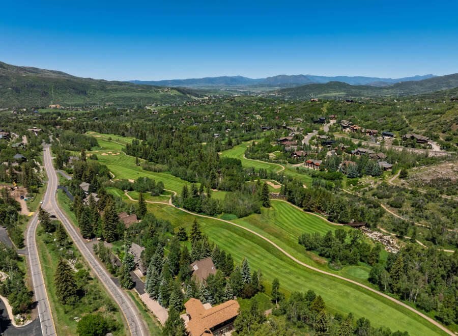 Experience luxury mountain living with this stunning aerial view of a sprawling estate nestled amidst a picturesque golf course and lush green hills.