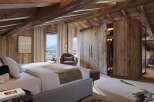 Experience luxurious mountain living in this stunning chalet bedroom, featuring exposed wooden beams and panoramic windows showcasing breathtaking snowy vistas.