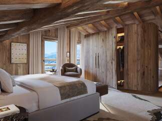 Experience luxurious mountain living in this stunning chalet bedroom, featuring exposed wooden beams and panoramic windows showcasing breathtaking snowy vistas.