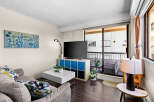 Bright and airy living room featuring a comfortable sofa with decorative pillows, a modern white coffee table, and a large flat-screen TV.