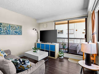 Bright and airy living room featuring a comfortable sofa with decorative pillows, a modern white coffee table, and a large flat-screen TV.