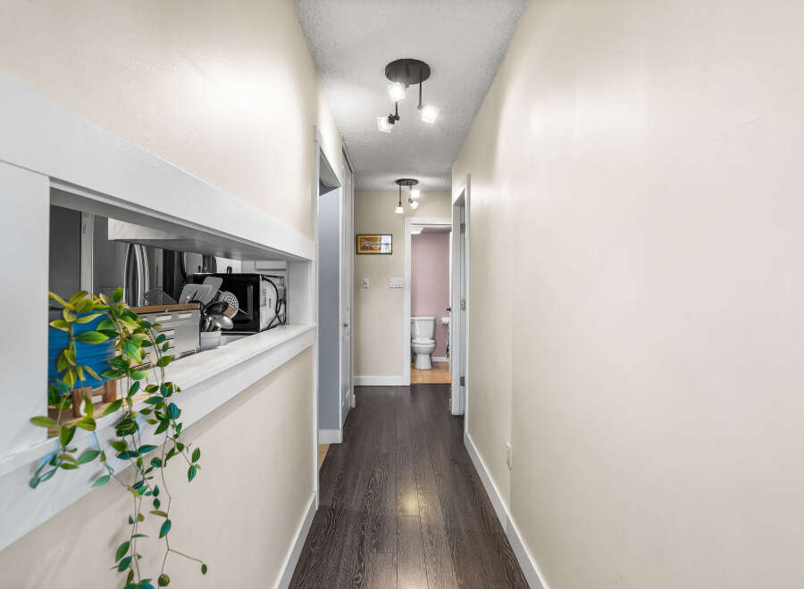 This hallway features a pass-through window with a plant and kitchen appliances visible.