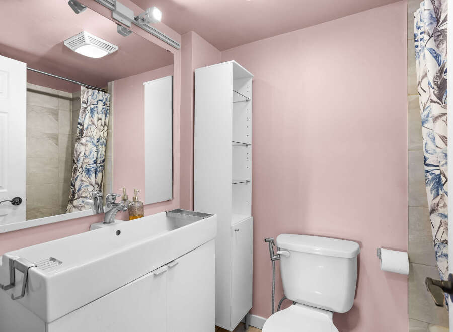 This charming bathroom features a modern white vanity with a sleek sink and chrome faucet, complemented by a tall white storage cabinet for ample space.